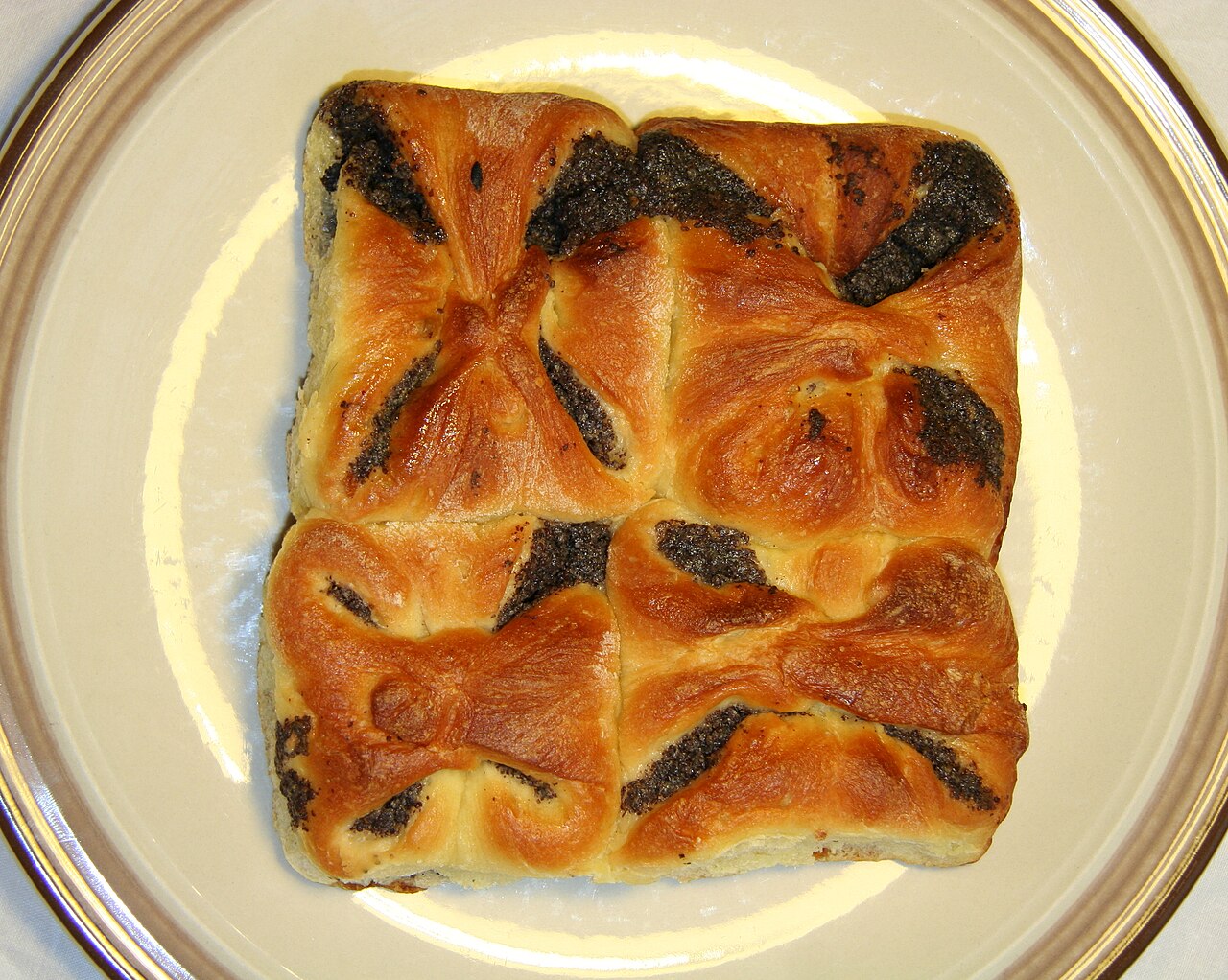 Four homemade poppy-seed kolaches arranged on a plate, each with a dark poppy-seed filling centered in golden pastry.