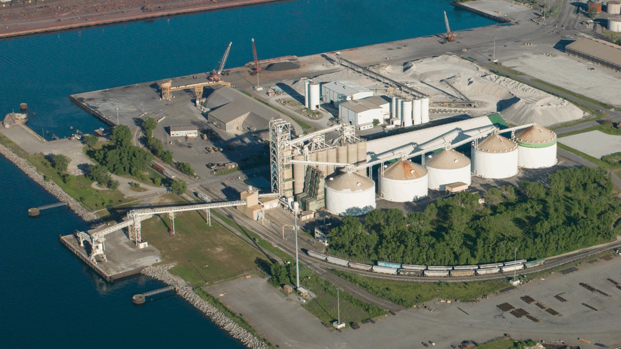 Aerial view of the Burns Harbor international grain terminal, with five white storage domes, conveyors and a loading pier on Lake Michigan