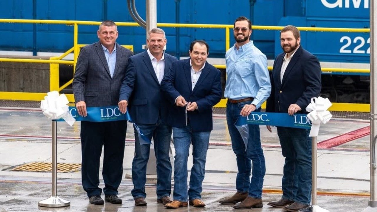 Five men in blazers and jeans hold a blue Louis Dreyfus Company ribbon in front of a blue locomotive as the man in the center holds scissors