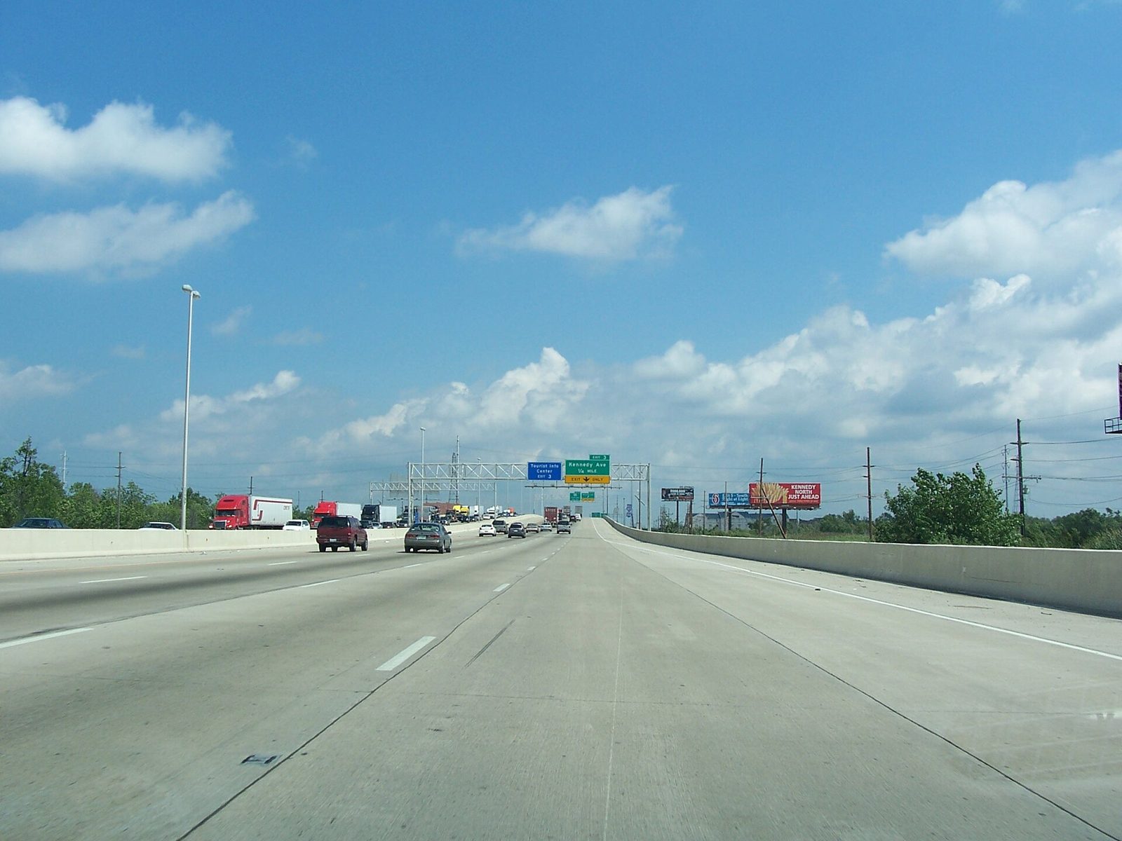 Wide concrete lanes of the eastbound Borman Expressway in Hammond under a blue sky, with trucks and overhead exit signs ahead
