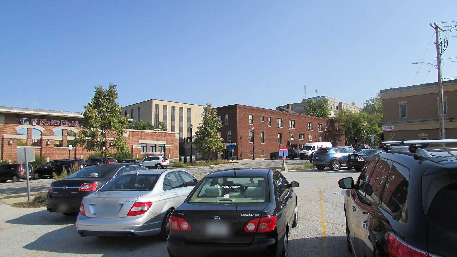 Cars in a surface parking lot near Courthouse Square in downtown Valparaiso, with brick office buildings behind.