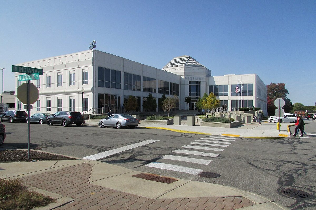 White two-story Porter County government building with a glass entrance and flags, seen across a crosswalk on Indiana Avenue