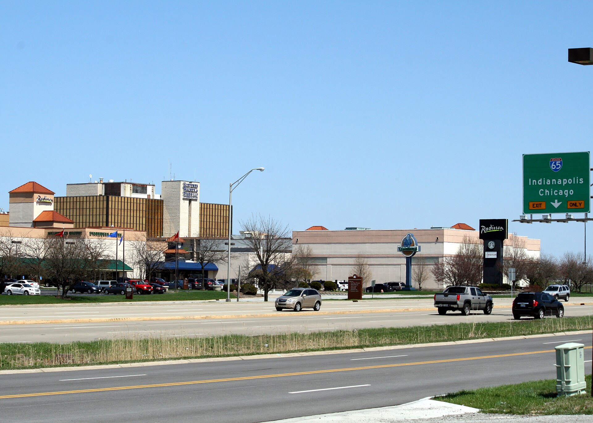 A wide highway in front of hotel and office buildings under a clear blue sky, with an Interstate 65 exit sign on the right